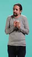 Vertical Man closes eyes while tasting and enjoying delicious coffee, isolated over blue studio backdrop. Person drinks caffeinated beverage to gain energy and be able to do doing productivity tasks, camera A video