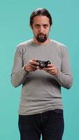 Vertical Portrait of man playing videogames holding controller, isolated over studio background. Gamer focused on gaming, participating in PvP online multiplayer game using console system, camera A video