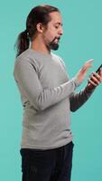 Vertical Joyous man with positive emotion enjoying talking with friends in phone call using smartphone, studio background. Happy person with smile on face, receiving good news during telephone call, camera A video
