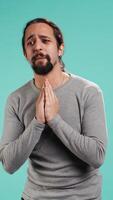Vertical Man putting hands together in begging gesture, making wish, asking for favor from friend, isolated over studio background. Desperate person asking for something, praying and hoping, camera B video