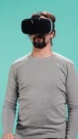 Vertical Tech enthusiast wearing virtual reality goggles, doing zooming in gestures. Arab man using high tech futuristic modern VR glasses, making tactile touching gesturing, studio background, camera B video