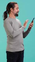 Vertical Man scrolling on smartphone touchscreen, using mobile phone to check social media feed, studio backdrop. Person browsing internet websites, isolated over studio background, camera A video