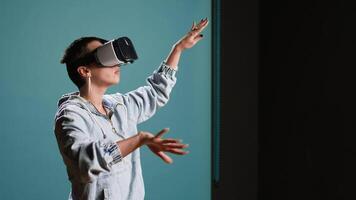 Groovy edgy woman wearing a 3d virtual reality headset in studio, using artificial intelligence and glasses against blue background. Modern funky girl with style uses a modern gadget. Camera A. video