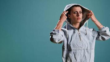 Bold serious woman putting her hood on and acting tough in studio, posing with arms crossed and showing confidence in her street style. Modern independent person acts as a gangster. Camera A. video