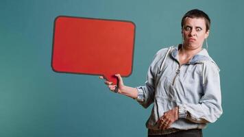 Casual person presenting an empty speech bubble sign in studio, working on a commercial with billboard icon. Woman holding cardboard for advertisement against background. Camera B. video