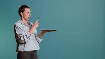 Modern tech person operating on tablet with a futuristic hologram, innovative visual graphics against blue background. Young woman looks at a holographic 3d image visualization. Camera B. video
