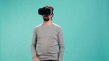 Man wearing virtual reality headset, interacting with interface, doing swiping motions. Person having fun using high tech futuristic modern VR gadget, isolated over blue studio background, camera B video