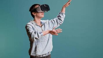 Groovy edgy woman wearing a 3d virtual reality headset in studio, using artificial intelligence and glasses against blue background. Modern funky girl with style uses a modern gadget. Camera B. video
