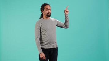 Portrait of smiling salesman pointing around with finger, doing recommendation, talking with audience. Happy person showing copy text space, doing advertisement, studio backdrop, camera A video