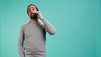 Man discussing with best friend over telephone call using smartphone, studio backdrop. Person talking with mate in phone call using cellphone, isolated over studio background, camera B video