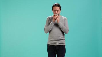 Man feeling tired, drinking coffee to wake up on his way to work. Exhausted person using caffeinated beverage to gain energy in the morning, blue studio background, camera A video