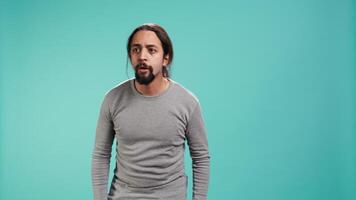 Portrait of frightened man covering his face with hands, standing isolated against studio background. Scared person with fearful facial expression suffering shock, feeling distraught, camera B video