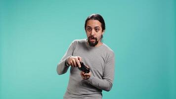 Gamer with disappointed look on face after receiving game over screen, holding controller. Man upset after losing videogame, playing with gamepad, isolated over studio background, camera B video