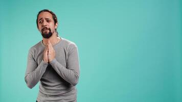 Man putting hands together in begging gesture, making wish, asking for favor from friend, isolated over studio background. Desperate person asking for something, praying and hoping, camera B video