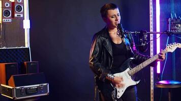 Female rock star singing a heavy metal song while playing her guitar for a music performance on stage. Loud edgy performer captivating the crowd with her iconic rebellious style. Camera A. video