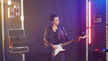 Confident musician performing live in a spotlight illuminated studio, surrounded by audio equipment and lights. Rocker doing a live performance in a rebellious style, bold attitude. Camera B. video