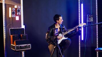 Professional artist instructor hosting a virtual singing lesson in studio, teaching people to sing and play guitar on online tutorial. Rock star doing live performance for training. Camera A. video
