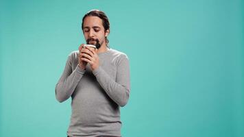Man feeling tired, drinking coffee to wake up on his way to work. Exhausted person using caffeinated beverage to gain energy in the morning, blue studio background, camera B video