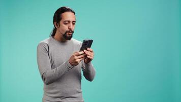 Man holding mobile phone, browsing betting website, celebrating after winning money, isolated over studio background. Cheerful person feeling happy while scrolling on smartphone, camera B video