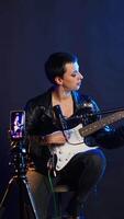 Vertical Musical instructor influencer creating content while playing guitar and singing alternative music, live audience online concert. Artist broadcasting her performance on streaming session. Camera B. video