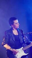 Vertical Punk rock girl with a grunge edgy style performing with a bass guitar in urban studio. Female rock star with bold attitude and fierce stage presence creating an iconic live performance. Camera A. video
