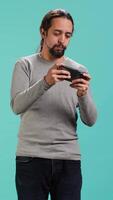 Vertical Man playing intense singleplayer videogames on smartphone, enjoying hobby. Gamer enjoying entertaining interactive game on phone, having fun, isolated over studio background, camera A video
