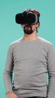 Vertical Man wearing virtual reality headset, interacting with interface, doing swiping motions. Person having fun using high tech futuristic modern VR gadget, isolated over blue studio background, camera B video