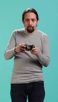 Vertical Upbeat person playing intense gaming console game, having fun, isolated over studio background. Joyous man pleased after being victorious in videogame, defeating all enemies using gamepad, camera A video