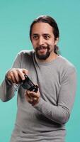 Vertical Cheerful player happy after winning gaming console game, shaking fist, studio background. Portrait of man satisfied after being victorious in videogame, defeating all enemies using gamepad, camera B video