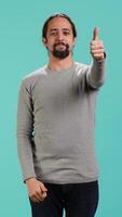 Vertical Portrait of upbeat man showing thumbs up sign gesturing, exulting happy facial expression and satisfaction. Jolly Arab person being excited, doing approving hand gesture, studio background, camera A video