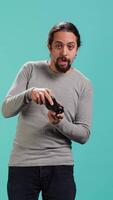 Vertical Gamer with disappointed look on face after receiving game over screen, holding controller. Man upset after losing videogame, playing with gamepad, isolated over studio background, camera A video