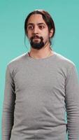 Vertical Portrait of serious Arab man standing isolated against blue studio background. Confident person having focused expression, suggesting determination and assertiveness, studio backdrop video