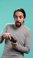 Vertical Gamer with disappointed look on face after receiving game over screen, holding controller. Man upset after losing videogame, playing with gamepad, isolated over studio background, camera B video