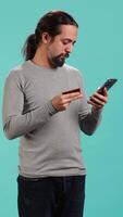 Vertical Elated man adding payment method on website, delighted to take advantage of promotions, studio background. Joyful person thrilled to do internet shopping, typing credit card data on phone, camera A video