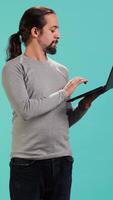 Vertical Portrait of smiling person spending time on laptop, isolated over studio background. Cheerful man checking social media posts on notebook, enjoying leisure time, camera A video