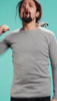Vertical Man jumping from joy in excitement while cheering for favorite sports team, studio background. Person celebrating after victory, showing intense enthusiasm, supporting team during game, camera B video