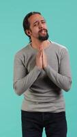 Vertical Man putting hands together in begging gesture, making wish, asking for favor from friend, isolated over studio background. Desperate person asking for something, praying and hoping, camera A video
