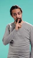 Vertical Annoyed man doing shushing hand gesturing, irritated by noise, having negative mood. Person placing finger on lips, doing quiet sign gesture, isolated over studio background, camera B video