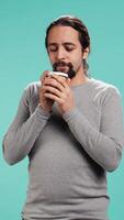 Vertical Man feeling tired, drinking coffee to wake up on his way to work. Exhausted person using caffeinated beverage to gain energy in the morning, blue studio background, camera B video
