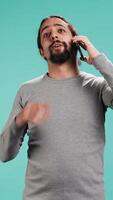 Vertical Joyous man catching up with friends in phone call using cellphone, studio background. Portrait of radiant person having conversation with mates during telephone call, camera B video