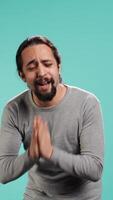 Vertical Man putting hands together in apology gesture, asking for forgiveness. Apologetic person doing sorry gesturing, asking for pardon, isolated over studio background, camera B video