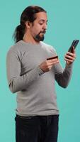 Vertical Man adding payment method on website, isolated over blue studio background. Cheerful person excited to do online shopping, carefully typing credit card information, camera A video
