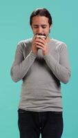 Vertical Man feeling tired, drinking coffee to wake up on his way to work. Exhausted person using caffeinated beverage to gain energy in the morning, blue studio background, camera A video