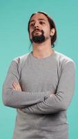 Vertical Grumpy man with sulking facial expression crossing arms, feeling annoyed, isolated over studio background. Portrait of irate person in bad mood feeling frustrated after argument, camera B video