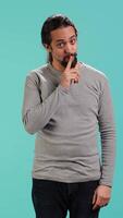 Vertical Annoyed man doing shushing hand gesturing, irritated by noise, having negative mood. Person placing finger on lips, doing quiet sign gesture, isolated over studio background, camera A video