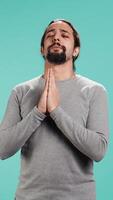 Vertical Pious man praying to his god, asking for forgiveness. Spiritual person doing worship hand gesturing, confessing, begging for pardon, isolated over studio background, camera B video