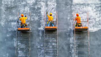 Three Construction Workers on Scaffolding Against a Gray Wall photo
