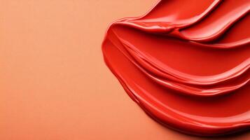 Swirls of rich coppery red liquid lipstick creating an abstract pattern on a soft muted orange background photo
