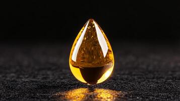 Golden facial oil drop glistening against a matte black background capturing light through its transparent form photo