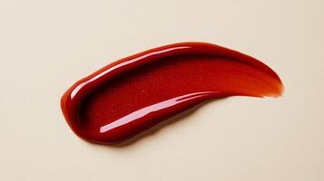Amber toned lip gloss smear with hints of red shimmer isolated on a soft muted cream background photo